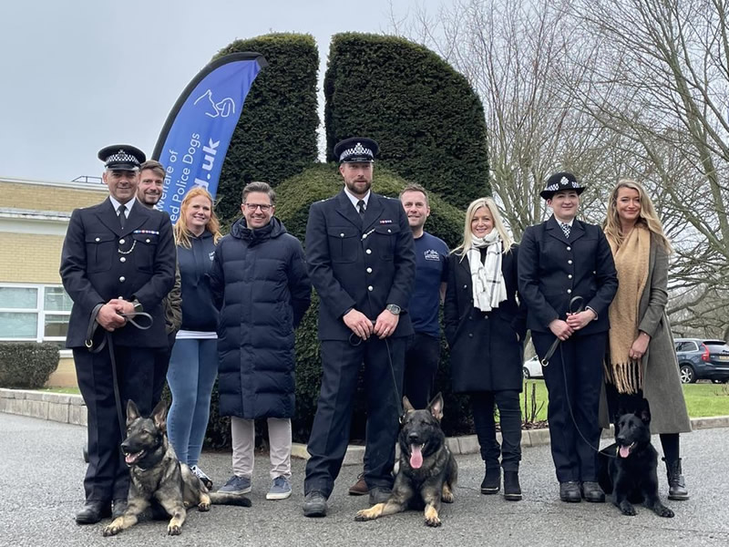 3 police dogs with their handlers, ambassadors and trustees in front of a hedge shaped like a dogs head